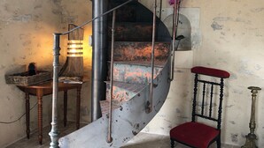 A spiral staircase with metal railings, a wooden table with a lamp, and a red cushioned chair.
