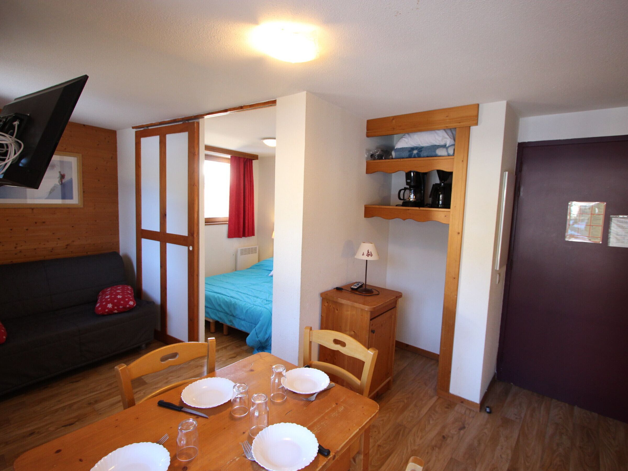 A compact room with a bed, a table set for dining, a sofa, and a TV mounted on the wall.