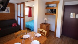 A compact room with a bed, a table set for dining, a sofa, and a TV mounted on the wall. - 2-Room Apartment Close to Slopes (Chamrousse)