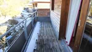 A wooden balcony with a metal railing, a glass door, and a view of a snowy landscape. - 2-Room Apartment Close to Slopes (Chamrousse)