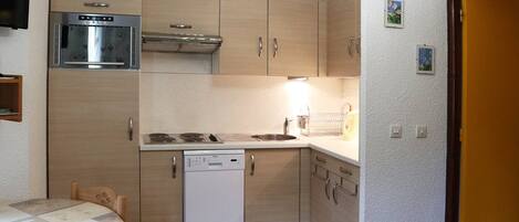 A compact kitchen with a built-in oven, a dishwasher, and wooden cabinets.