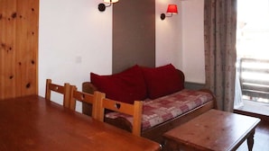 Una habitación acogedora con una mesa de madera, un sofá con cojines rojos, dos lámparas de pared y una ventana con cortinas.