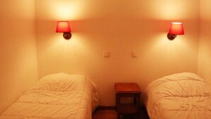 Una habitación con dos camas, una mesita de noche y dos lámparas fijadas a la pared.