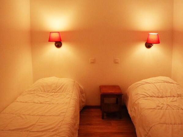 A room with two beds, a nightstand, and two wall-mounted lamps.