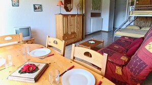 A cozy living room with a wooden table, chairs, a sofa, a TV, and a cabinet. - Studio for 4 people at the foot of the slopes near shops (Chamrousse)