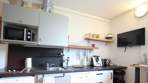 A compact kitchen with a microwave, sink, and a coffee maker. There are cabinets, a small refrigerator, and a TV mounted on the wall. - Cozy 19m² studio at the foot of the slopes with pool (Chamrousse)