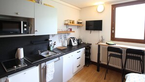 A compact kitchen with a microwave, stove, sink, and a small dining area with chairs and a table. - Cozy 19m² studio at the foot of the slopes with pool (Chamrousse)