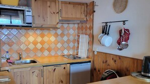 Una cocina compacta con armarios de madera, un microondas integrado y un lavavajillas.