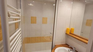 Un baño moderno con ducha de vidrio, tocador de madera con lavamanos y espejo sobre el lavamanos.