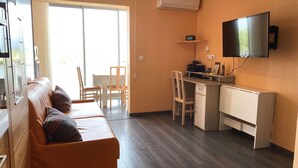 A compact living space with a sofa, a small desk, and a television mounted on the wall.