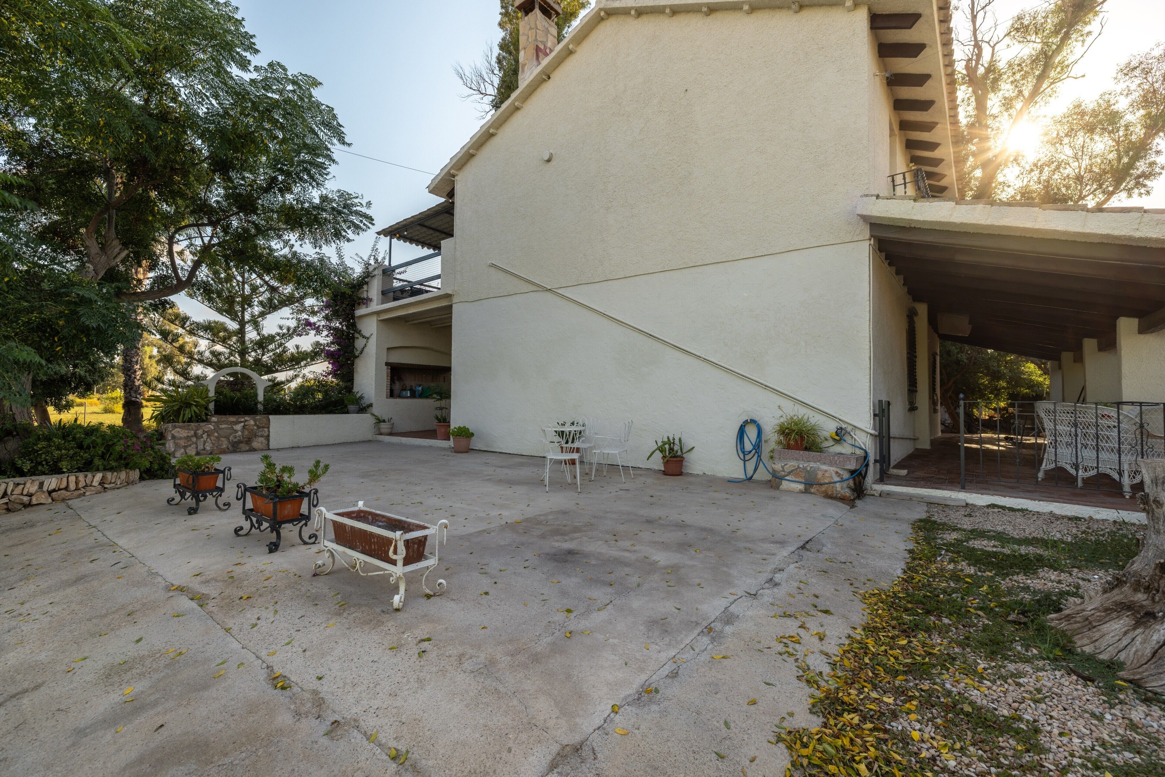 A covered patio area with outdoor furniture, potted plants, and a concrete floor.