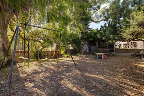 Un jardin avec une balançoire, une table de pique-nique et un petit espace de jeux.