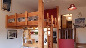 A bunk bed with a kitchen area below, a dining table with chairs, and a staircase leading to another level.