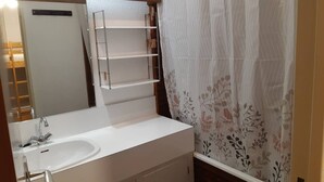 A bathroom with a white sink, a mirror, and a shelf unit.