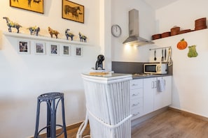 A kitchen with white cabinets, a microwave, and a stove. There are decorative plates on the wall and a clock. - Studio Apartment 'Estudio La Cochera' with Shared Pool, Wi-Fi, and Air Conditioning. (Deltebre)