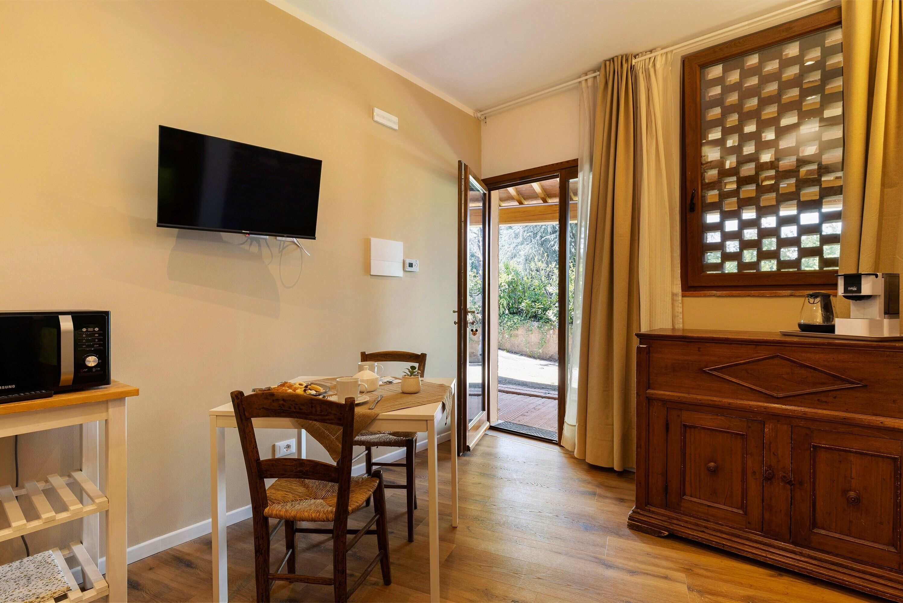 A room with a TV, a microwave, a dining table with chairs, a wooden cabinet, and a sliding glass door leading to an outdoor area.