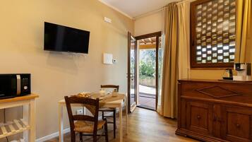 A room with a TV, a microwave, a dining table with chairs, a wooden cabinet, and a sliding glass door leading to an outdoor area.