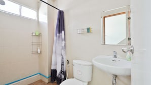 Een badkamer met douche, toilet, wastafel en raam.