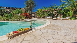 Un espace piscine doté d’une terrasse en pierre, de chaises longues et d’une variété de plantes tropicales.