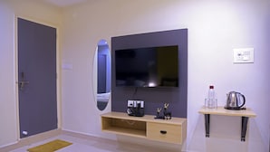 Quarto de hotel moderno com televisão de tela plana na parede, mesa de consola de madeira com chaleira e copos, e um pequeno espelho na parede.