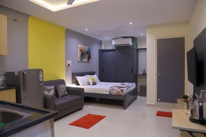 Une chambre d’hôtel moderne équipée d’un lit, d’un canapé, d’un petit coin cuisine et d’une télévision.
