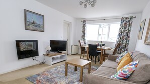 A living room with a sofa, a coffee table, a TV, and a dining area with chairs and a table. - Beachcombers, 13 Chesil House (Bridport)
