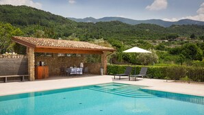 Une piscine agrémentée d’une pergola et de coins salon extérieurs, entourée d’une végétation luxuriante et avec des montagnes en toile de fond.