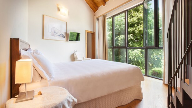 Une chambre à coucher avec un grand lit, une table de chevet avec une lampe, un tableau encadré et un téléviseur fixé au mur.