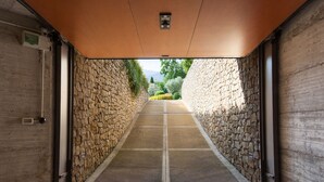 Un couloir aux murs de pierre et au sol carrelé, qui mène à un espace extérieur agrémenté de verdure et offrant une vue sur le ciel.
