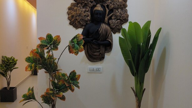 A hallway with a Buddha statue, potted plants, and a light switch on the wall. - Modest Rooms by LIBRA (Kharar)