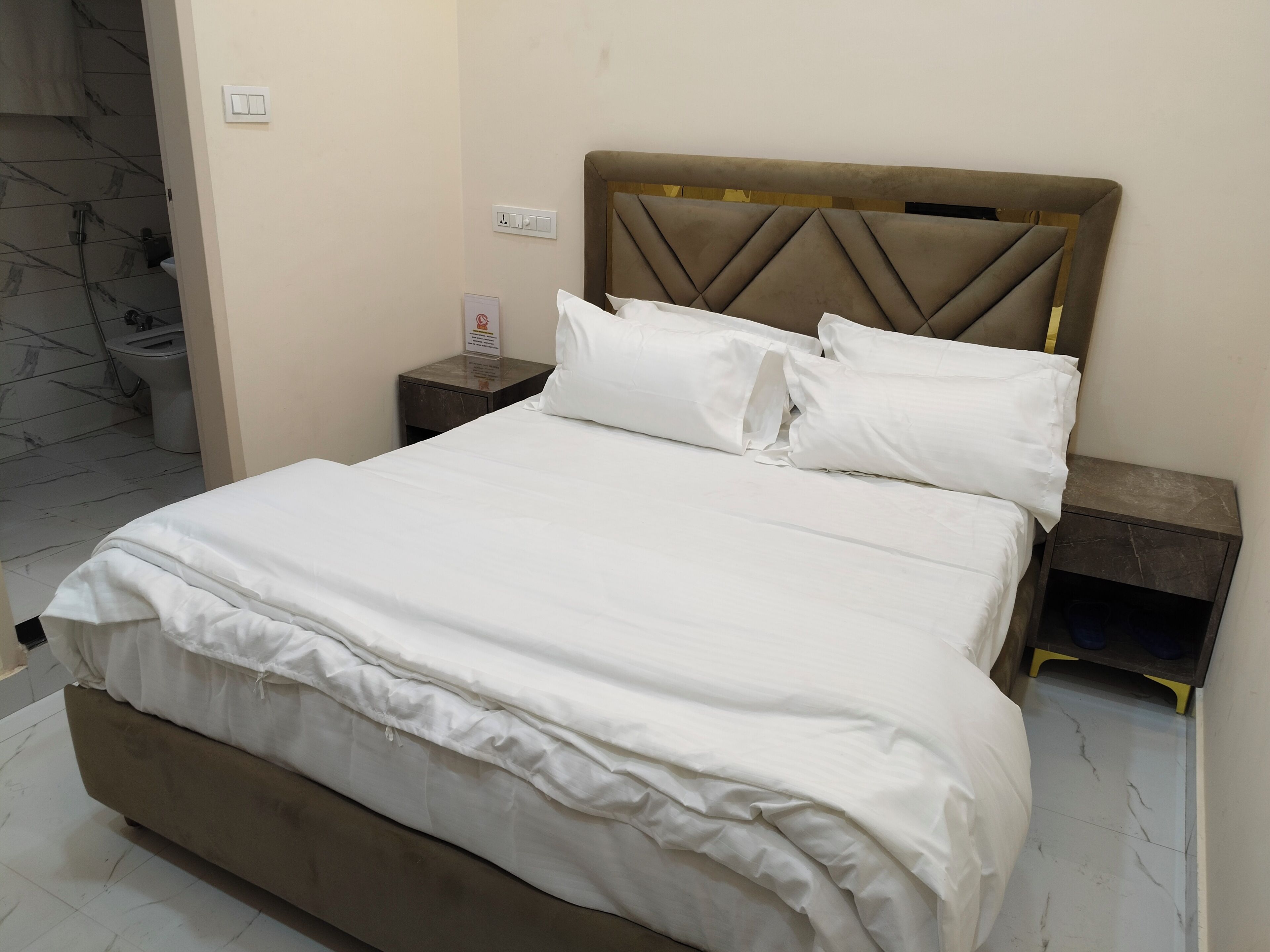 A neatly made bed with white linens, a padded headboard, and a bedside table with a lamp.