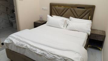 A neatly made bed with white linens, a padded headboard, and a bedside table with a lamp.