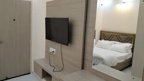 A modern hotel room with a large mirror, a flat-screen TV mounted on the wall, a wooden bench, and a bed with a headboard. - Modest Rooms by LIBRA (Kharar)