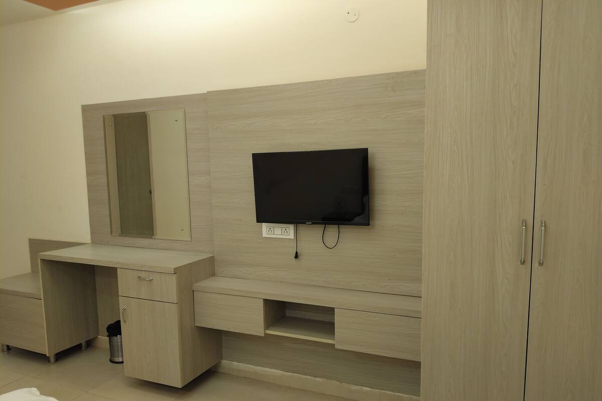 A modern bathroom with a wooden vanity, a mirror, a flat-screen TV mounted on the wall, and a cabinet with drawers.