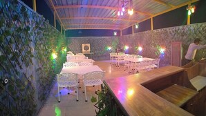 An outdoor dining area with white tables and chairs, surrounded by decorative foliage and walls. - Modest Rooms by LIBRA (Kharar)