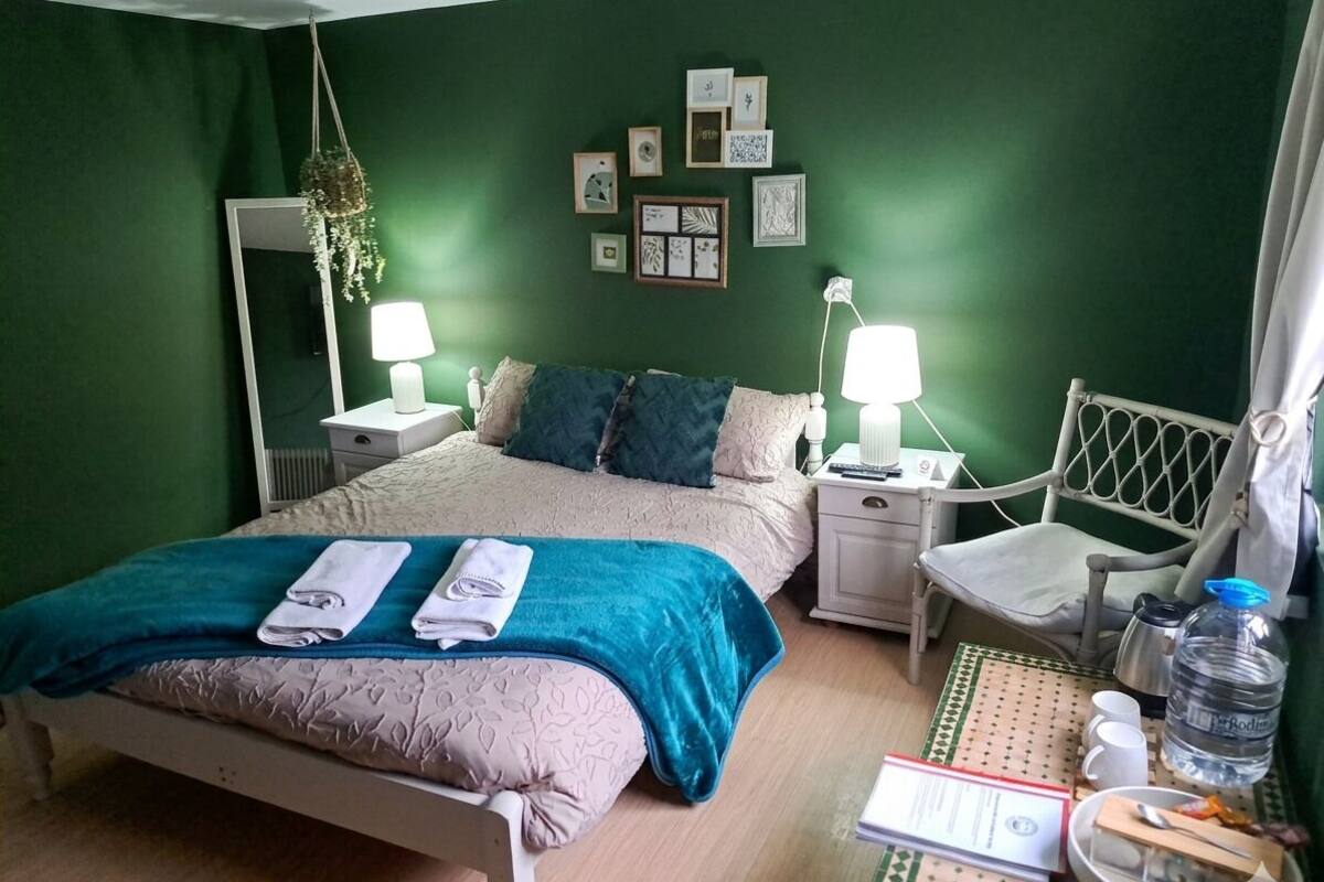 A bedroom with a bed, bedside tables, a chair, a mirror, wall art, and a table with a water bottle and a tray.