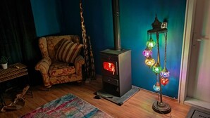 A room with a wood-burning stove, a patterned armchair, a colorful rug, and a decorative hanging light fixture. - Muddy Puddles Farm (Kovachevets)