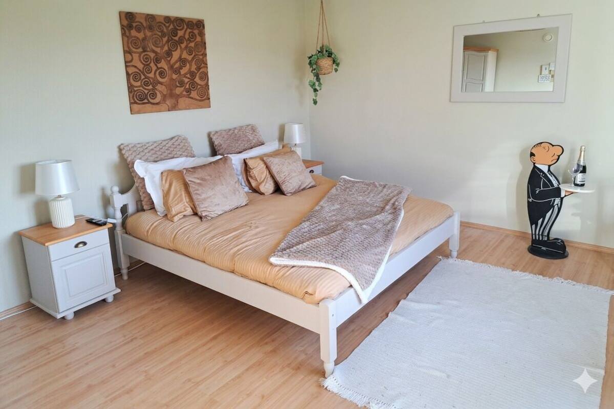 A bedroom with a bed, bedside tables, a hanging plant, a mirror, and a statue.