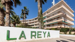 Un edificio de varios pisos con balcones, palmeras y un letrero que dice 'LA REYA'.