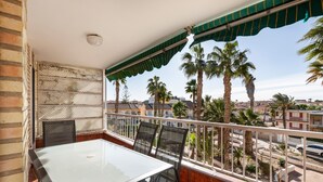 Un balcón con una mesa y sillas de vidrio, con vistas a palmeras y edificios.