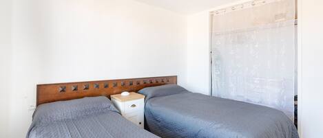 A bedroom with two beds, a wooden headboard, a bedside table, and a curtain with a pattern.