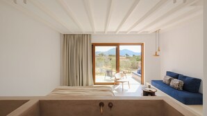 Un dormitorio moderno con un ventanal grande, una bañera, un sofá azul y vistas a las montañas.