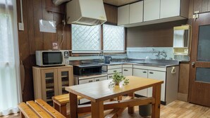 A compact kitchen with wooden cabinets, a microwave, a sink, and a dining table with benches. - One-room private inn Koropokkuru (中富良野町字中富良野東１線)