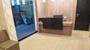 A reception area with a wooden desk, a brown sofa, and a large window with a sign advertising rooms for rent. - Tag my stay mist (Chennai)