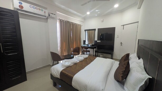 A hotel room with a bed, two chairs, a desk, a TV, and an air conditioning unit. - Tag my stay mist (Chennai)