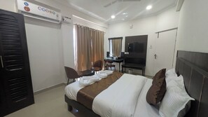 A hotel room with a bed, two chairs, a desk, a TV, and an air conditioning unit. - Tag my stay mist (Chennai)