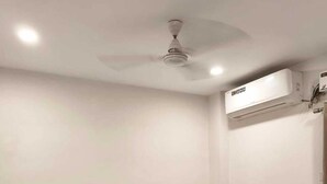 A neatly made bed with white and brown bedding, a dark headboard, a bedside table, and an air conditioning unit on the wall. - Tag my stay mist (Chennai)