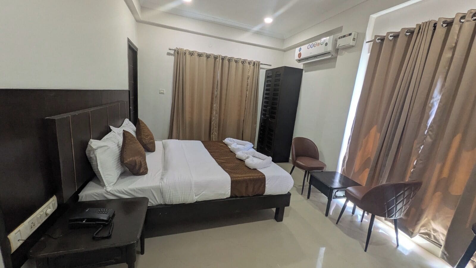 Ein Hotelzimmer mit Bett, Schreibtisch mit Telefon, Stuhl und Klimaanlage.