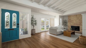 Een ruime woonkamer met een blauwgroene deur, een open haard en een groot raam.