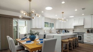 Een moderne keuken met witte kasten, een houten eettafel en barstoelen.